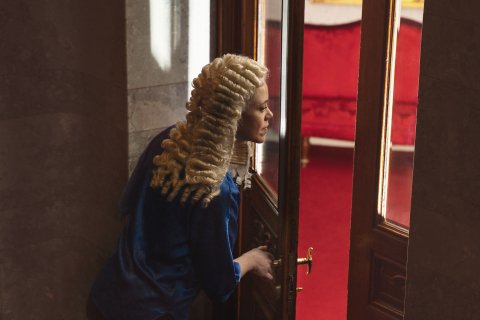 Person med Holbergparykk titter inn gjennom dør