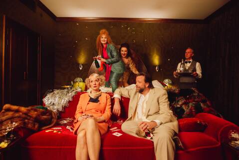 Fire skuespillere som herjer på et hotellrom. To kvinner hopper i senga, mens en kvinne og en mann sitter i sofaen